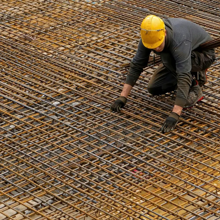 Trabajador con casco amarrando la malla de acero de un radier