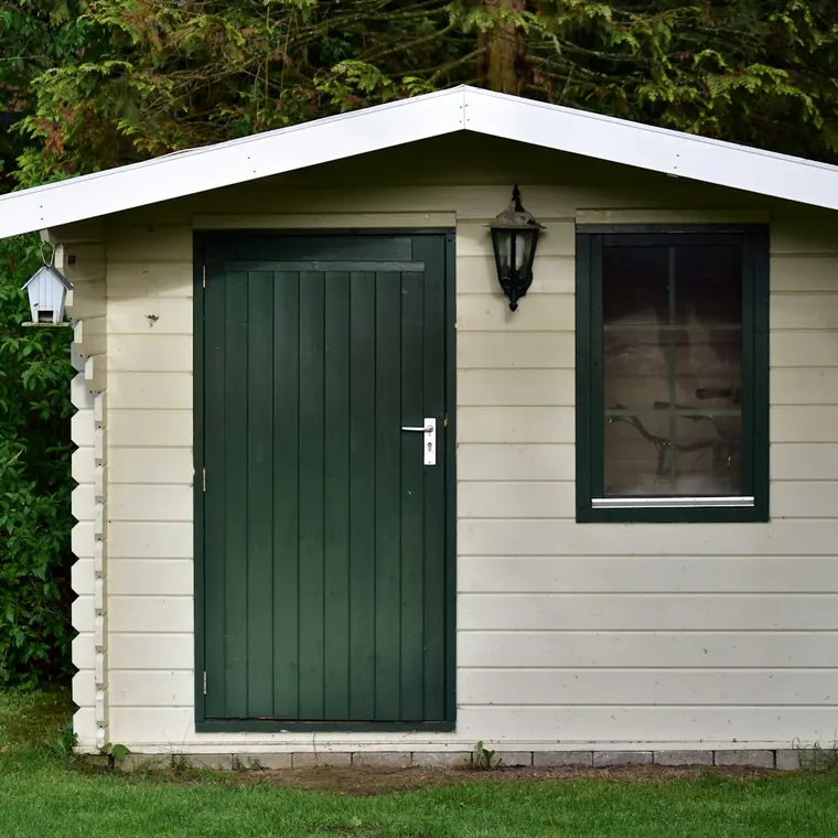 Bodega prefabricada de madera con puerta verde en un jardín